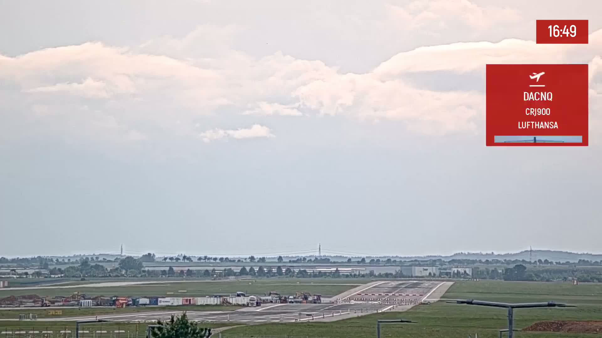 An airport runway with some construction equipment visible under a partly cloudy sky.