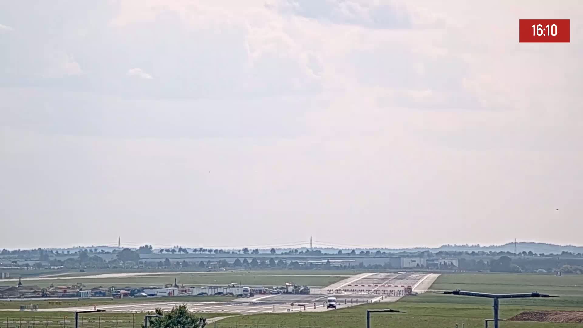 A long runway at an airport is visible under a mostly cloudy sky.