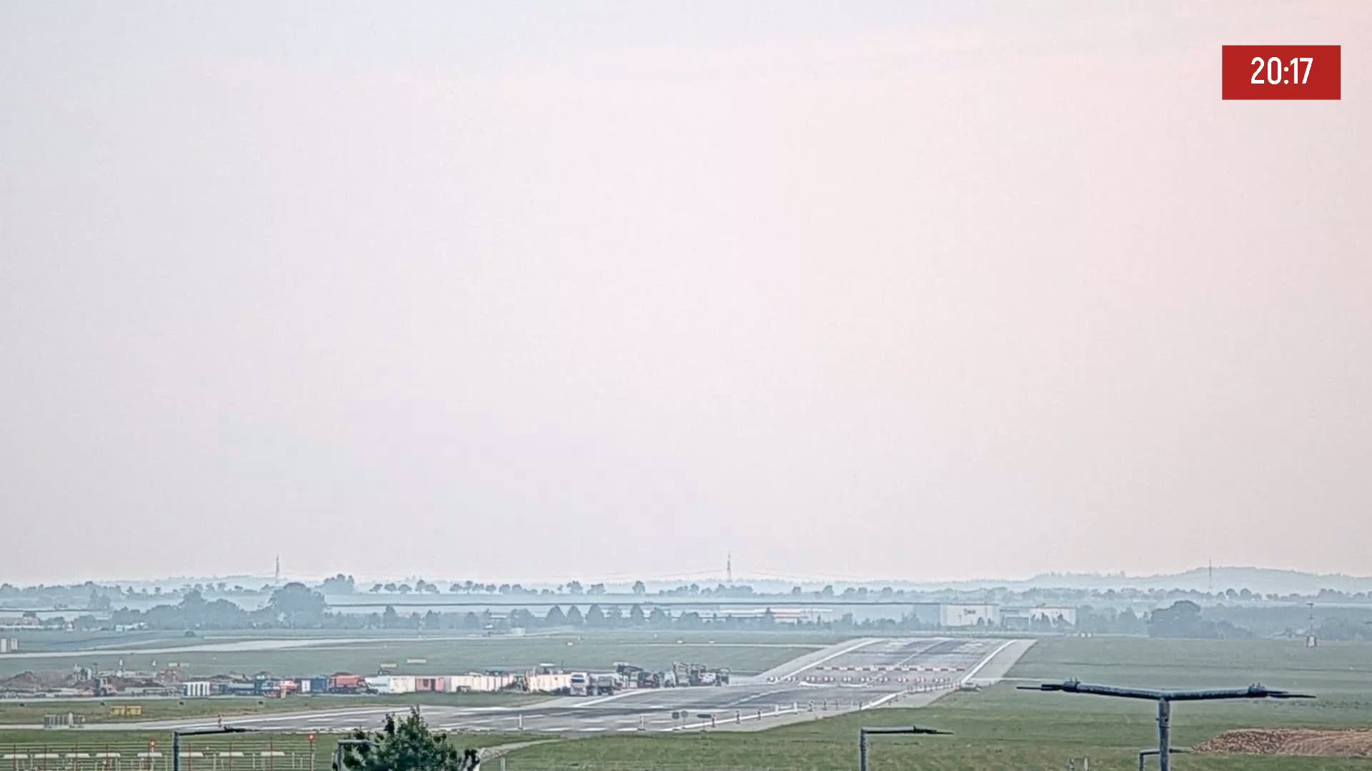 A hazy view of an airport runway with some construction equipment visible in the foreground and a distant horizon.
