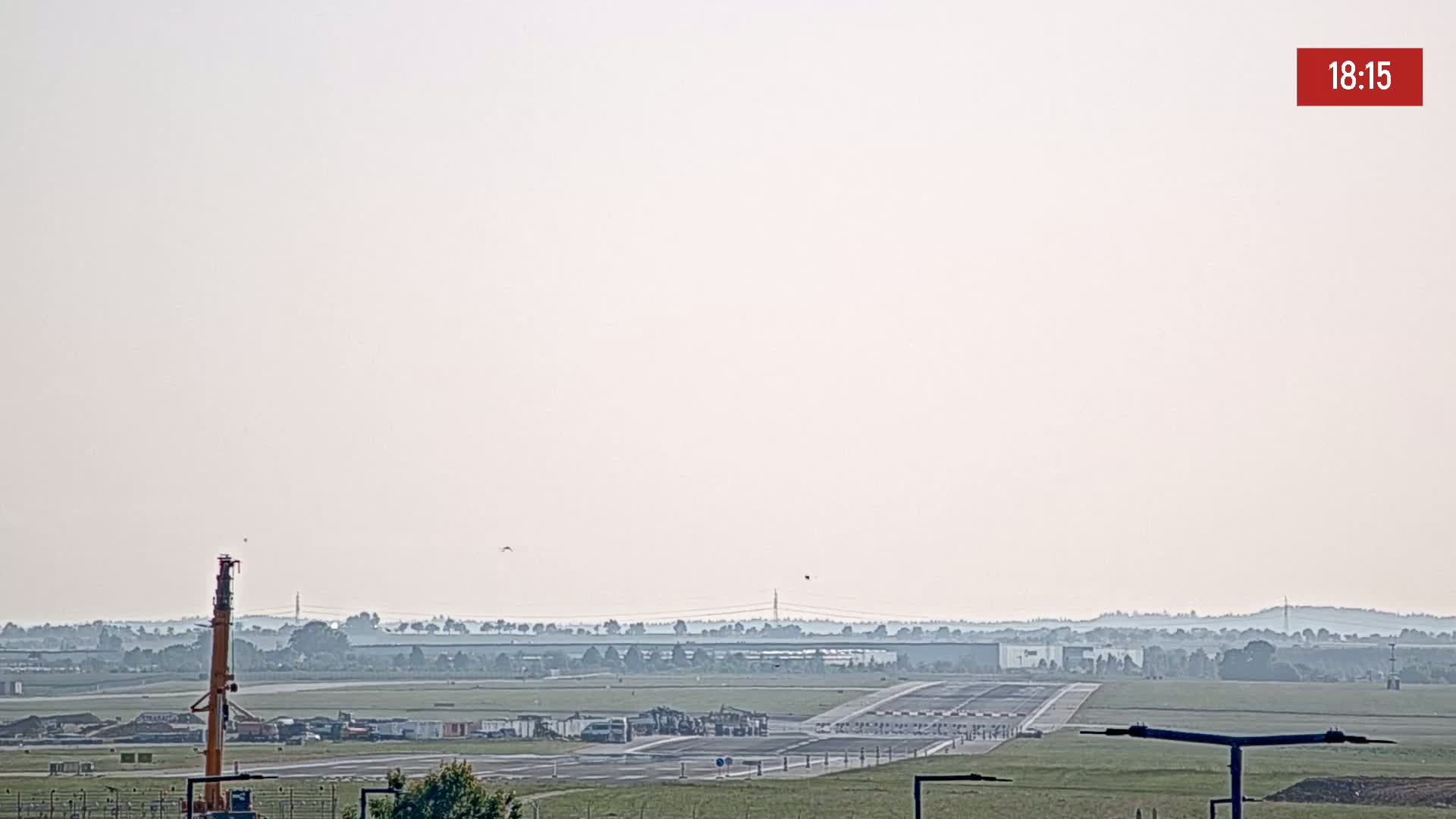 A hazy view of an airport runway with construction equipment and vehicles visible, under a light, hazy sky.