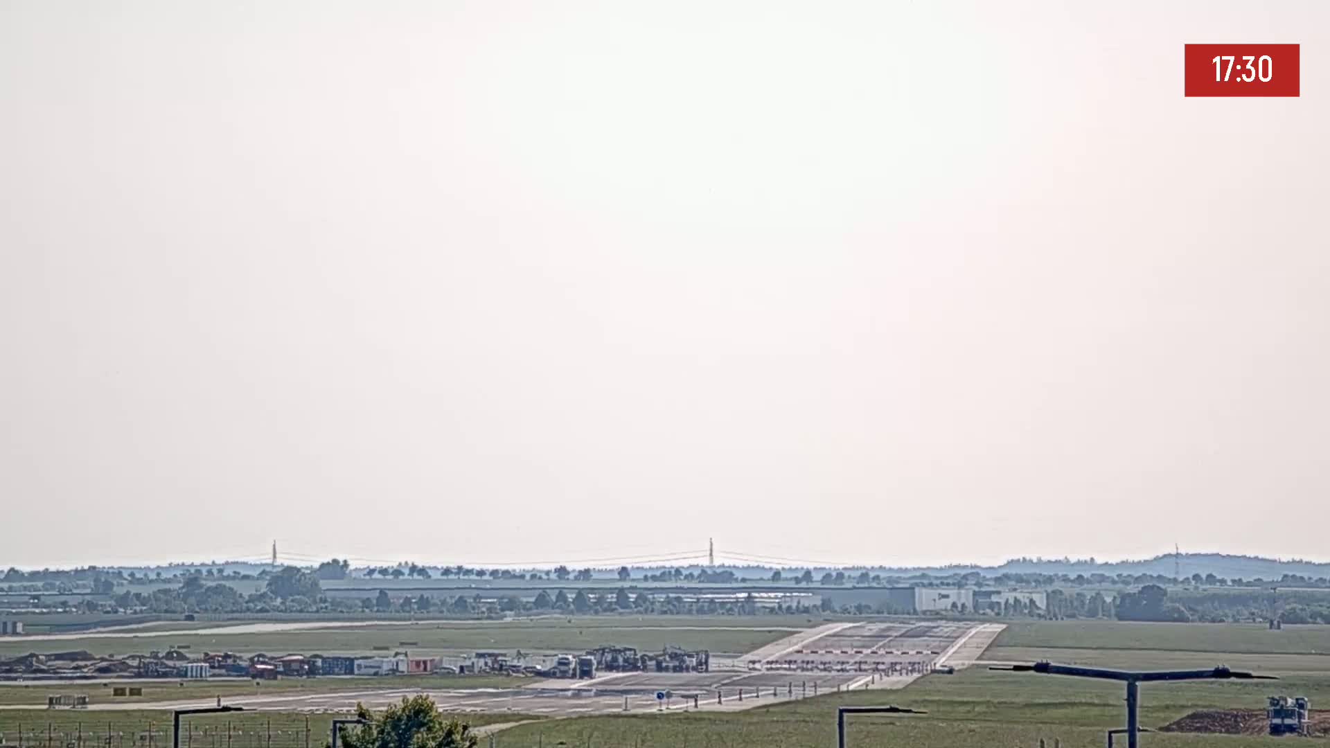 A hazy, sunny day reveals an airport runway with construction equipment and vehicles near the terminal.