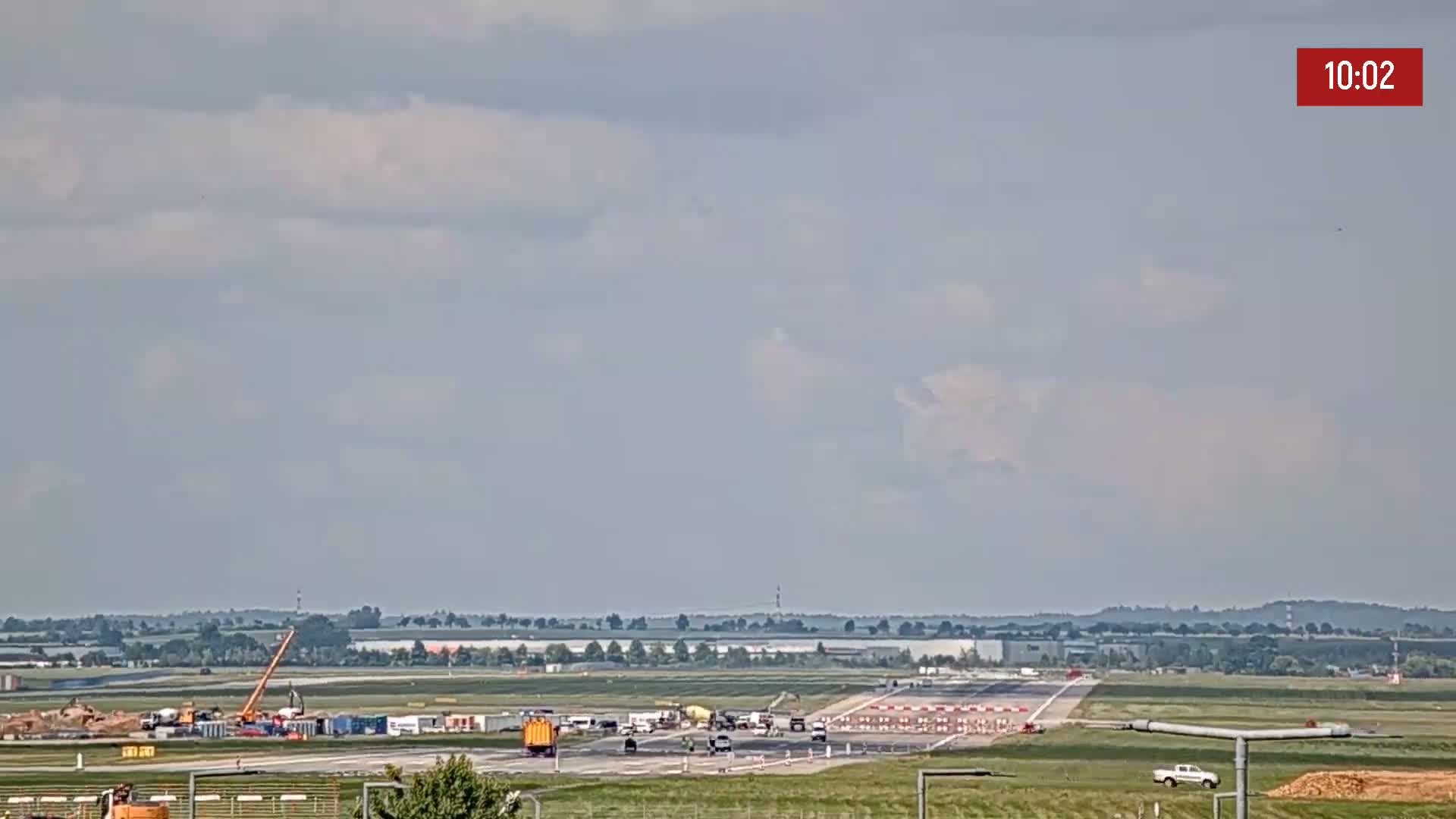 A mostly cloudy sky overlooks an airport runway with construction equipment and vehicles present.