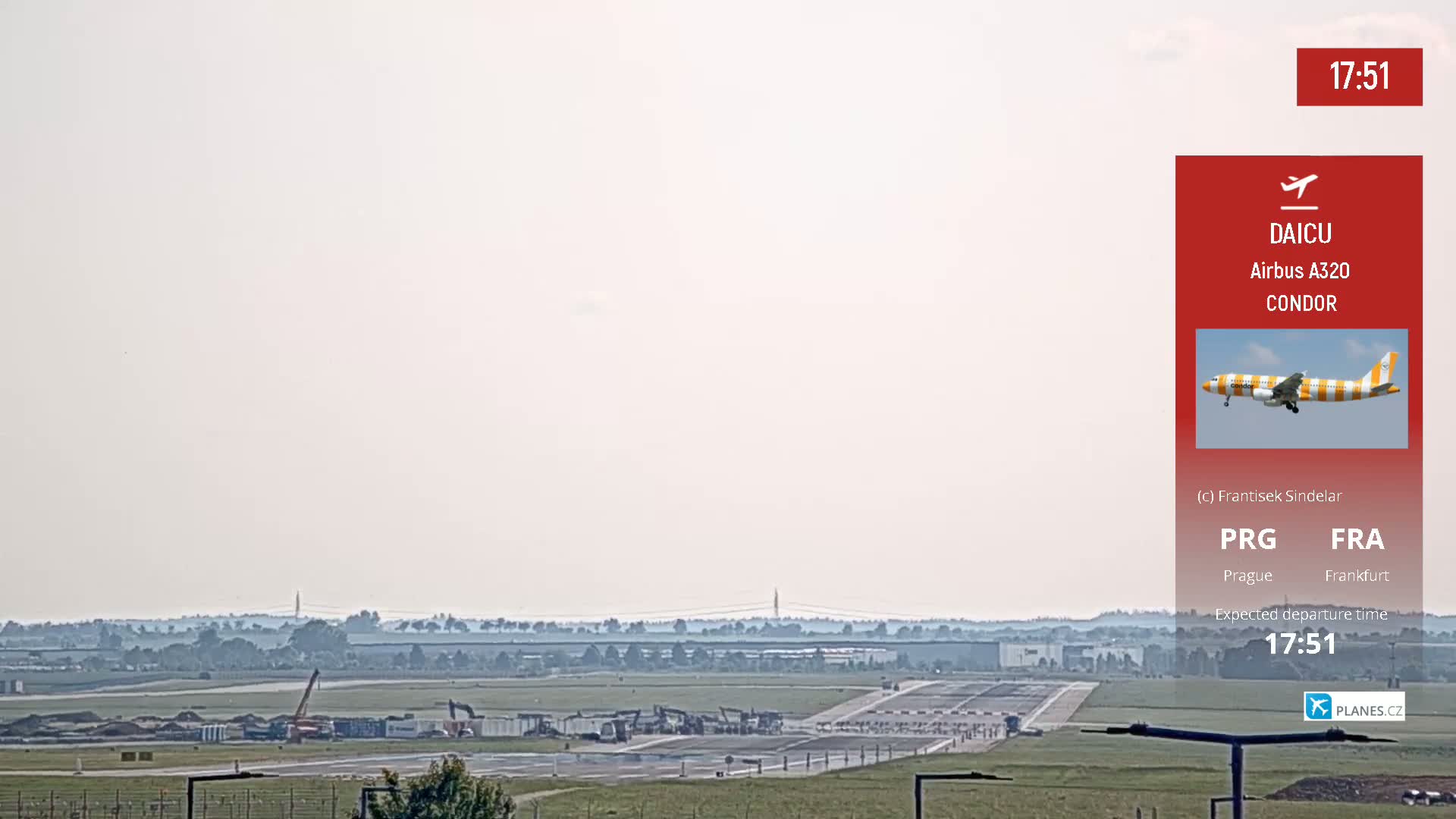 A hazy view of an airport runway with construction equipment and a distant airplane in flight.