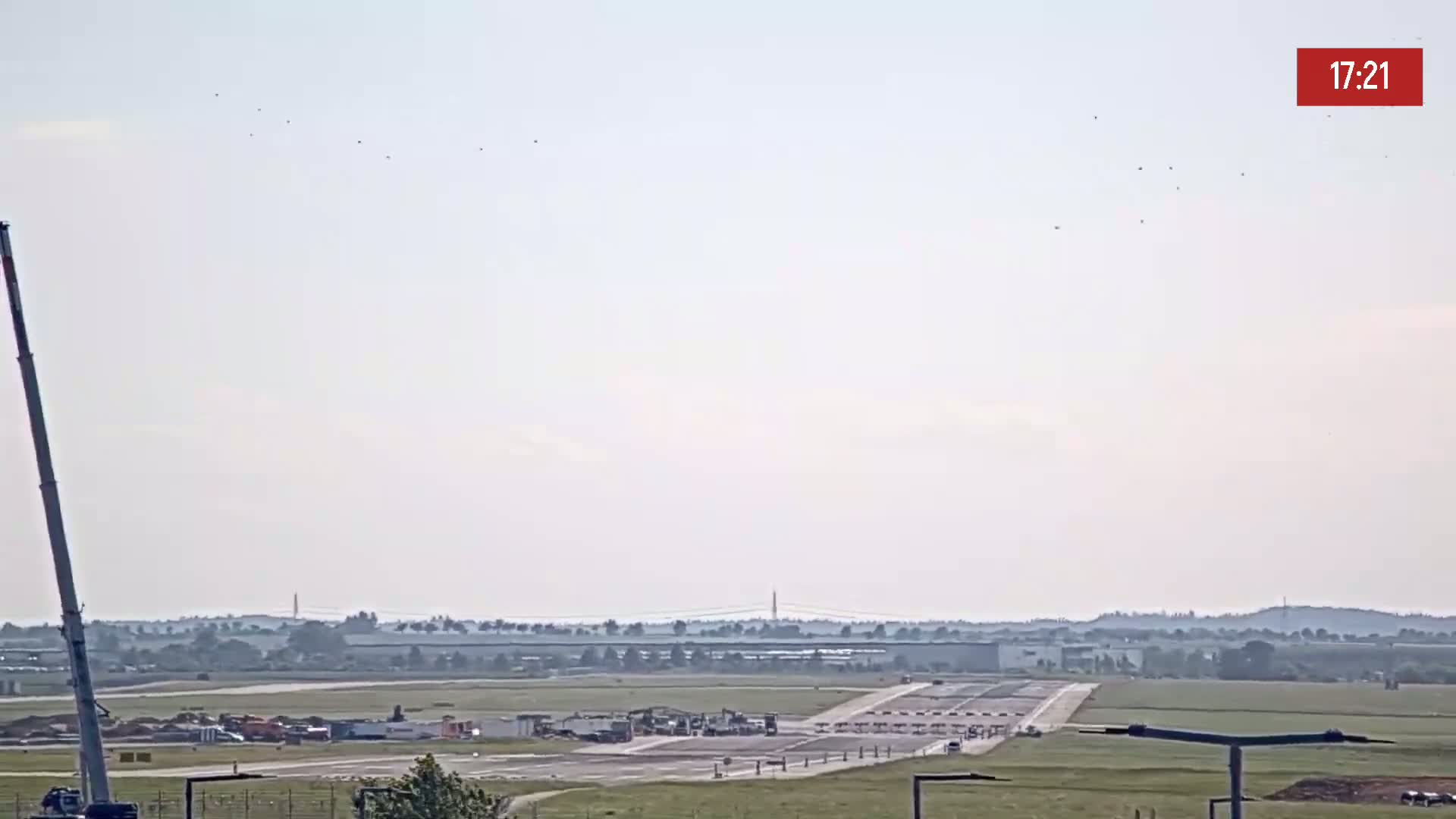 A long crane is visible to the left of a hazy, sunny day view of an airport runway undergoing construction.