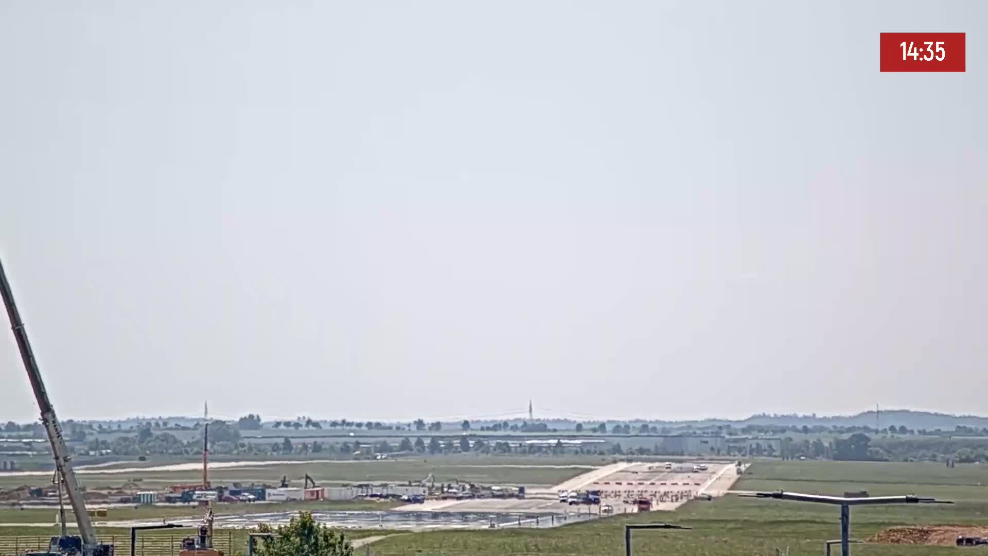 A long runway under construction is visible on a hazy day, with several vehicles and construction equipment present.