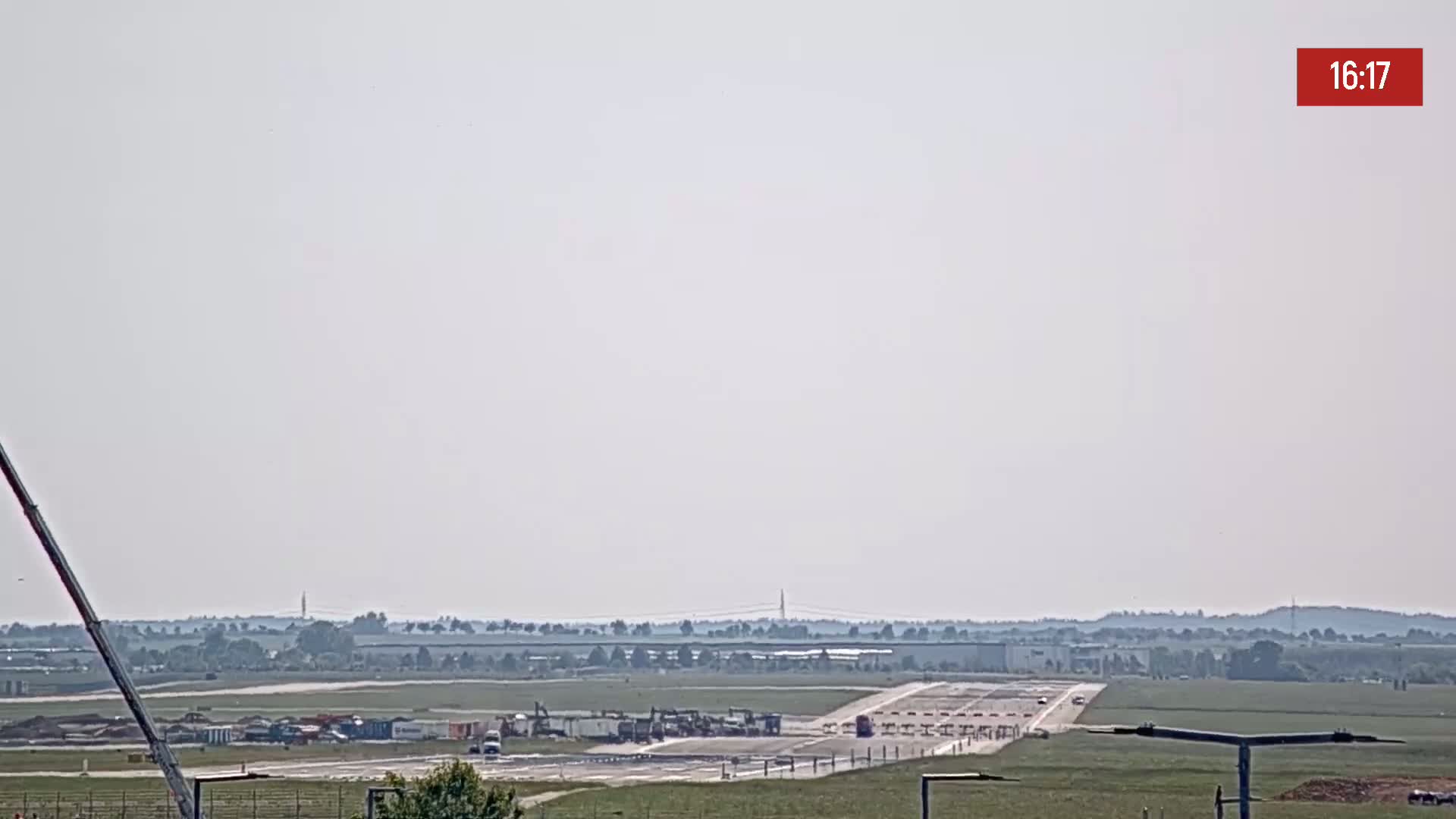 A hazy, sunny day shows an airfield with construction equipment and vehicles near a runway.