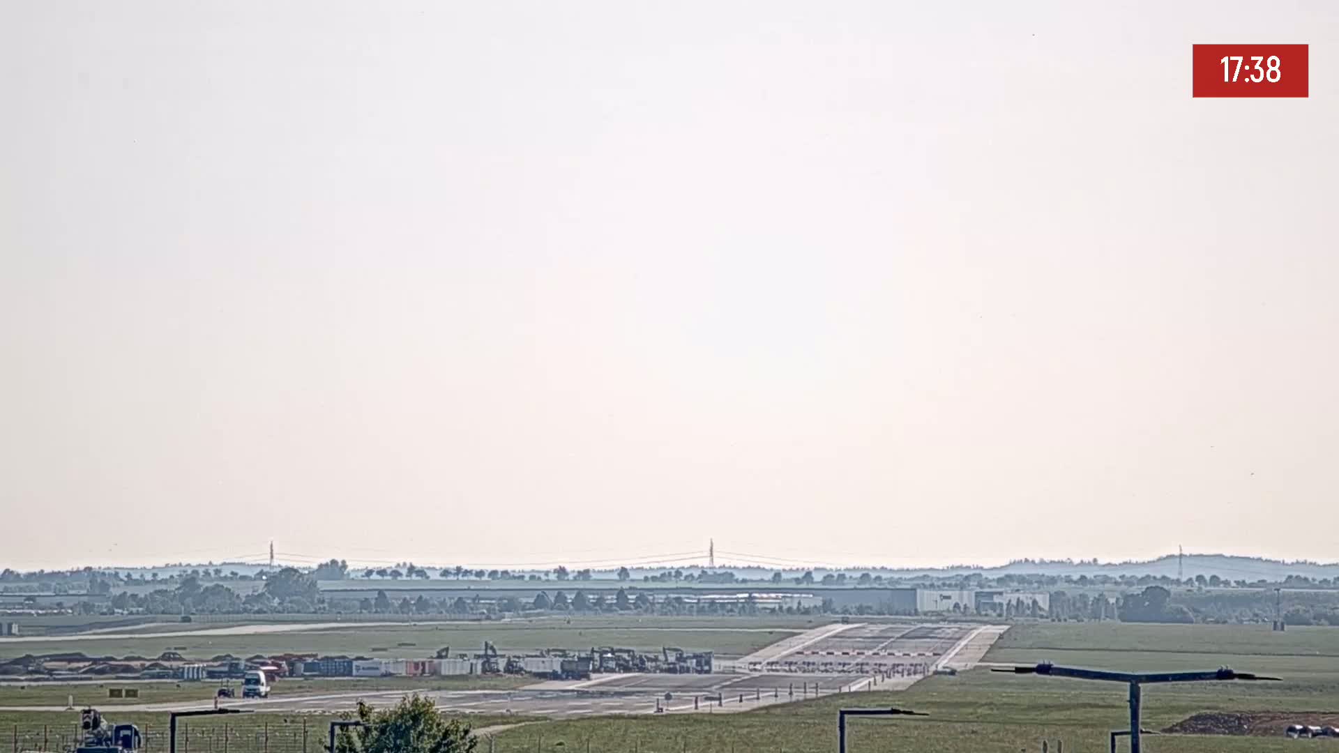 A hazy view of an airport runway with construction equipment and vehicles present.
