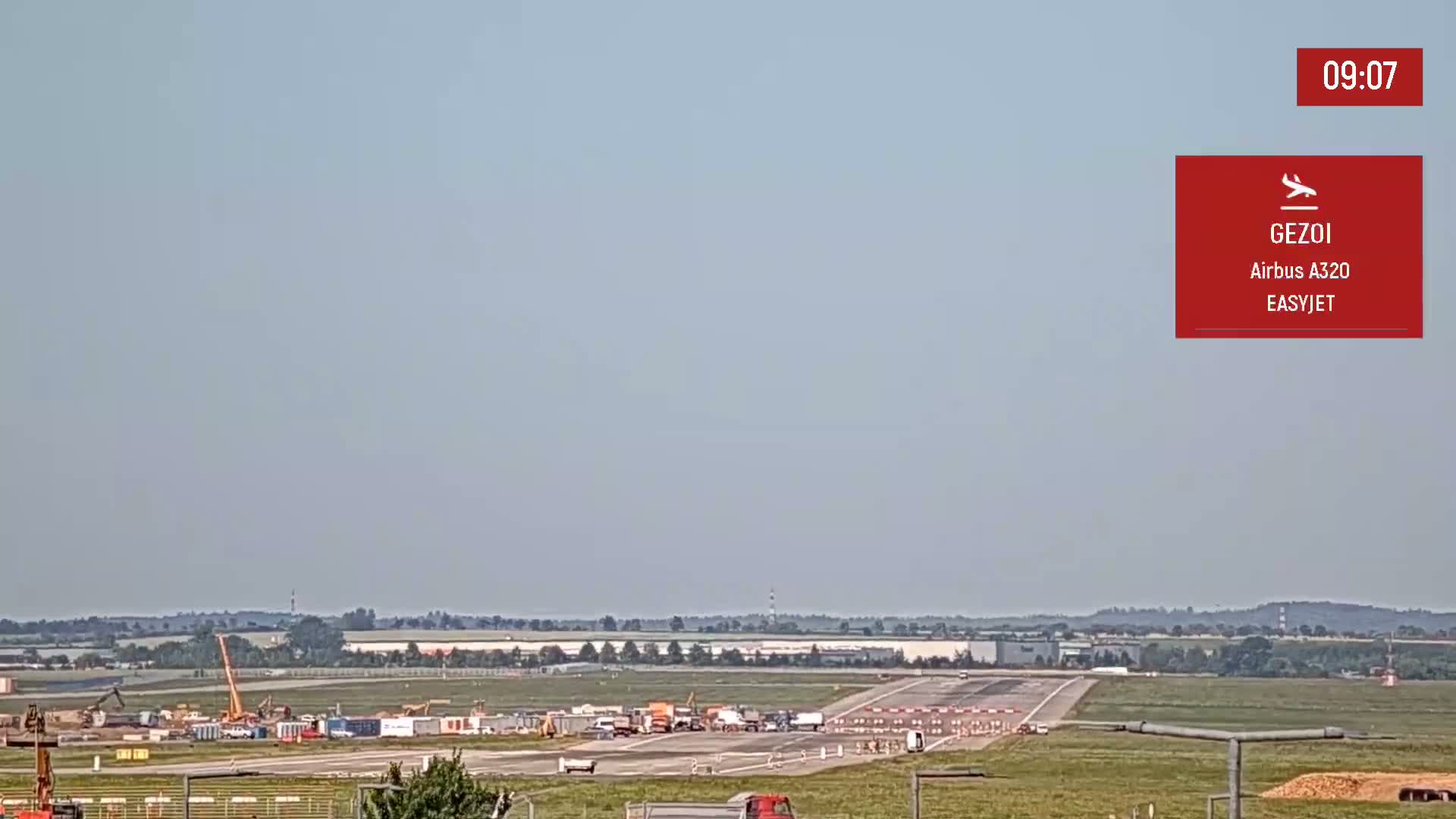 Under a clear sky, an airport runway shows construction activity with several vehicles and equipment present.
