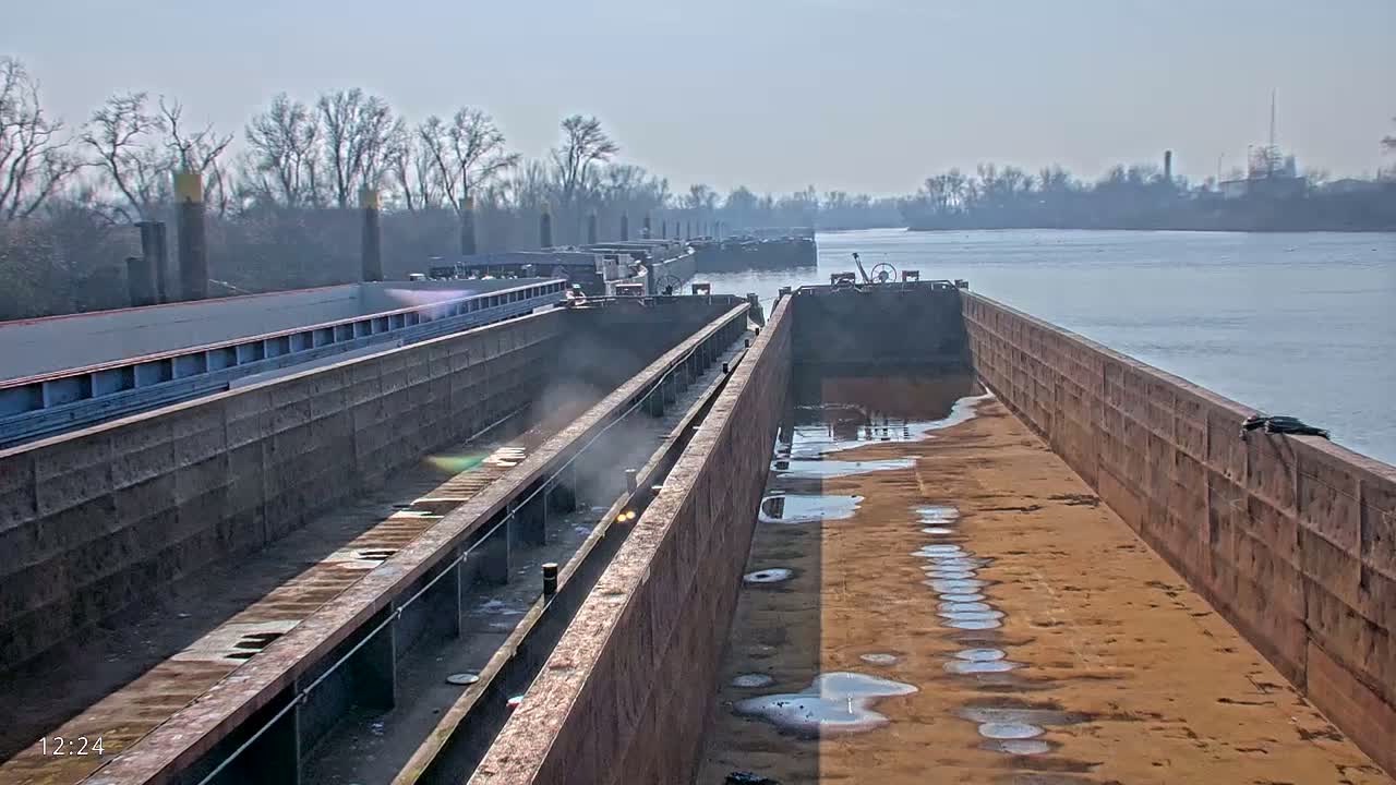 Several empty barges are moored along a riverbank on a clear, sunny day.