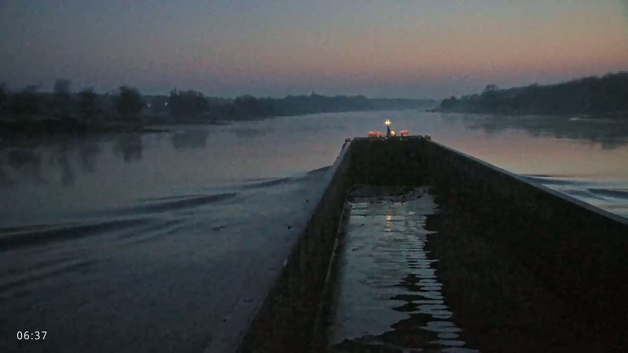 A barge moves down a calm river at twilight under a dusky pink and gray sky.
