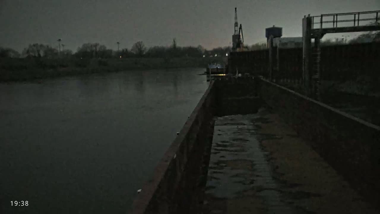 A barge is moored alongside a riverbank at dusk or dawn, under a dark, overcast sky.