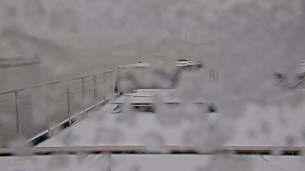 A snow-covered barge is seen through a snow-covered window, with another barge visible in the distance.