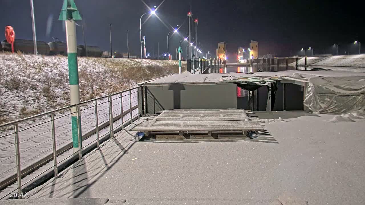 A snow-covered barge is moored at a lock, with lights illuminating the scene at night.