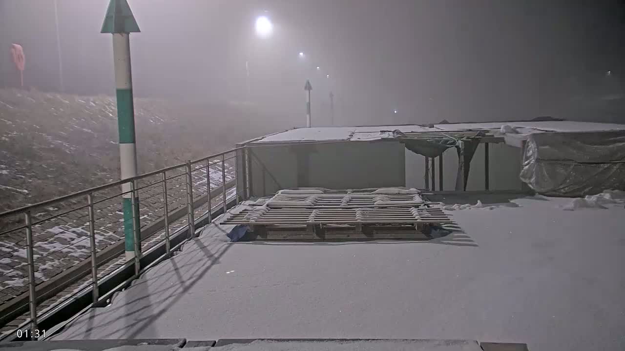 A snow-covered platform with a wooden pallet and a partially enclosed structure is visible in foggy nighttime conditions.