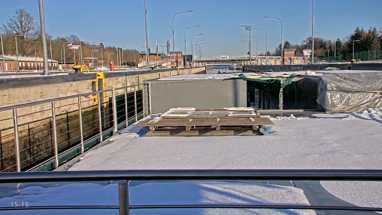 A snow-covered deck of a boat is situated in a canal lock on a sunny day.