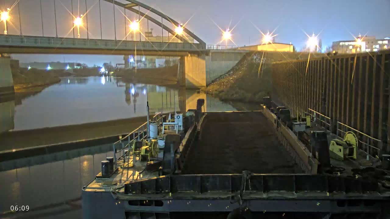 A barge filled with dark material is moored under a bridge at night, with lights illuminating the scene.