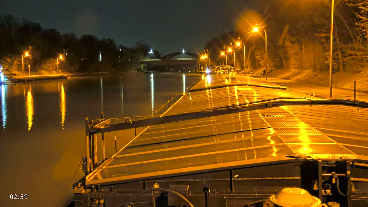 A barge illuminated by streetlights travels down a canal at night.
