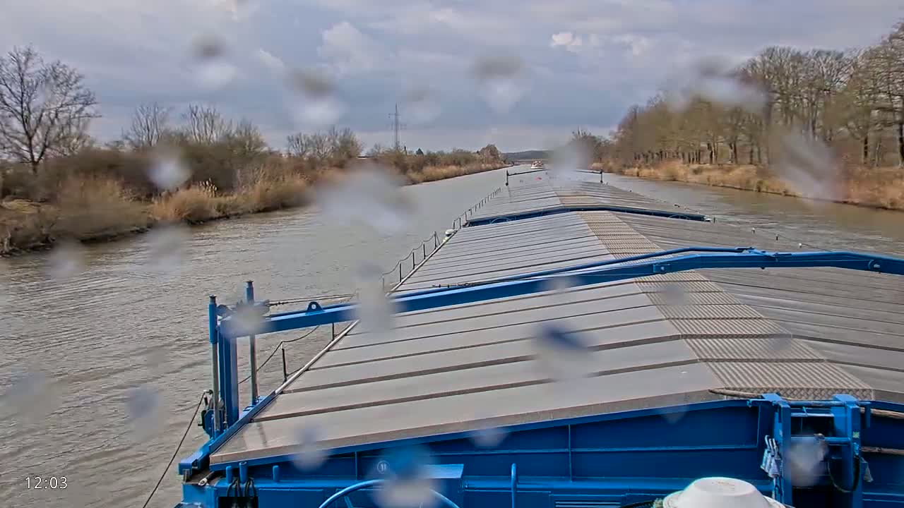 A blue barge travels down a canal on an overcast day, rain drops obscuring the view.