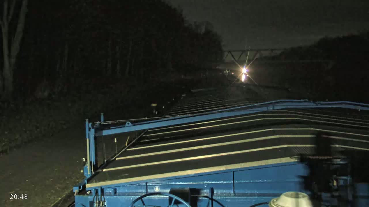 A blue barge's deck is visible at night, with a distant light source ahead and dark trees lining the sides.