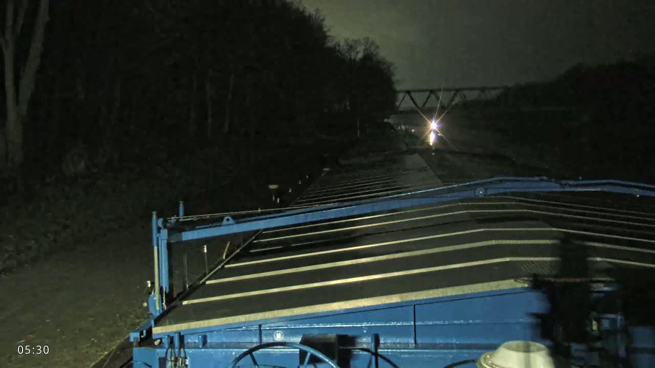 A blue barge's deck is visible at night, with dark trees and a distant bridge faintly illuminated in the background.