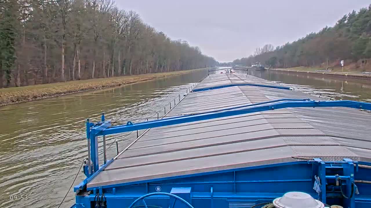 A blue barge travels down a canal lined with bare trees on an overcast day.