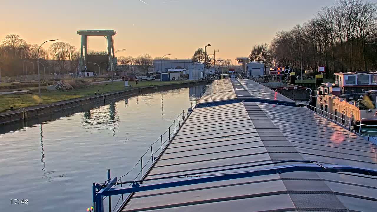 A barge travels down a canal at sunset, passing by other docked barges and a lock system.