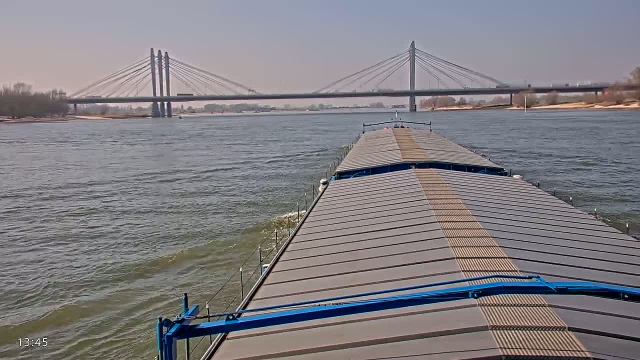 A barge travels on a river under a cable-stayed bridge on a partly sunny day.