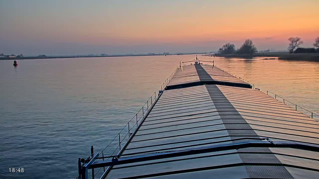 A barge travels down a wide river at sunset under a calm, clear sky.