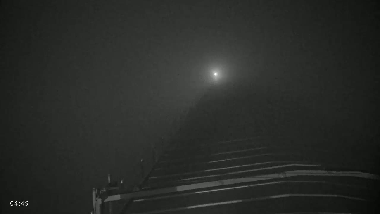 A bright light is visible through heavy fog in the distance, above a dark, sloped structure with horizontal lines.