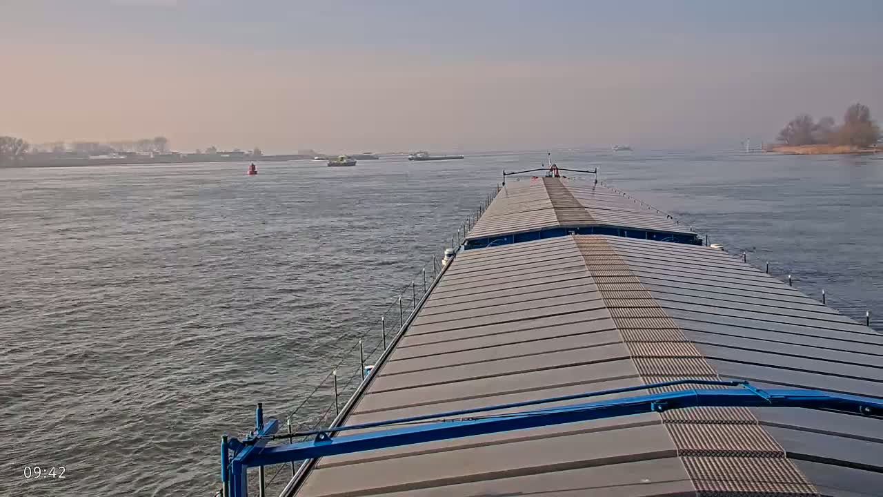 A barge travels down a wide river on a hazy day, with other vessels visible in the distance.