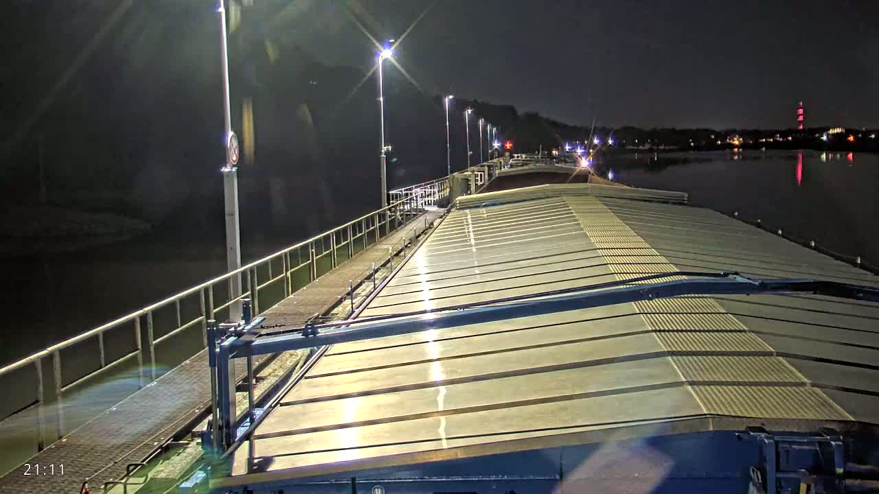 A barge's deck is illuminated at night by several lights along a waterway.