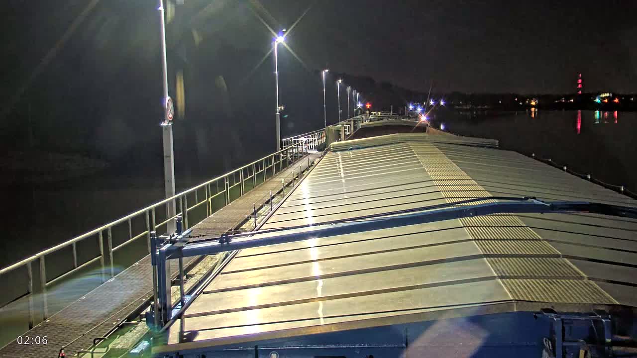 At night, a barge's deck is illuminated by lights along a railing overlooking dark water.