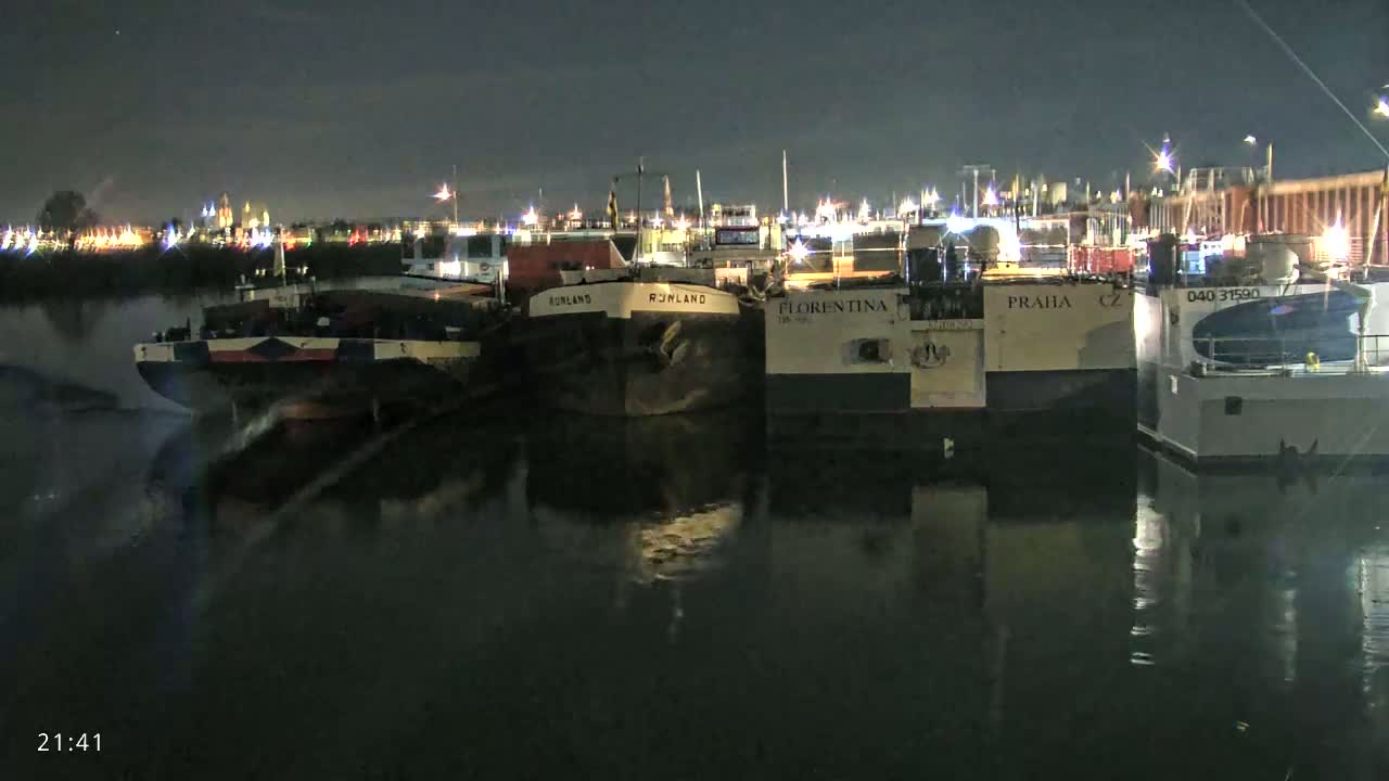 Several barges are moored at a dock at night, their reflections visible in the dark water.