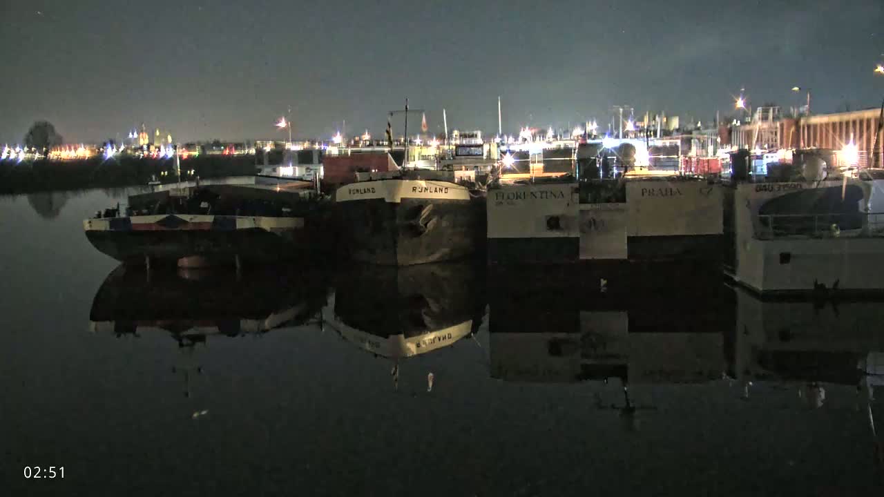 Several barges are moored along a dark waterway at night, their reflections visible in the calm water.