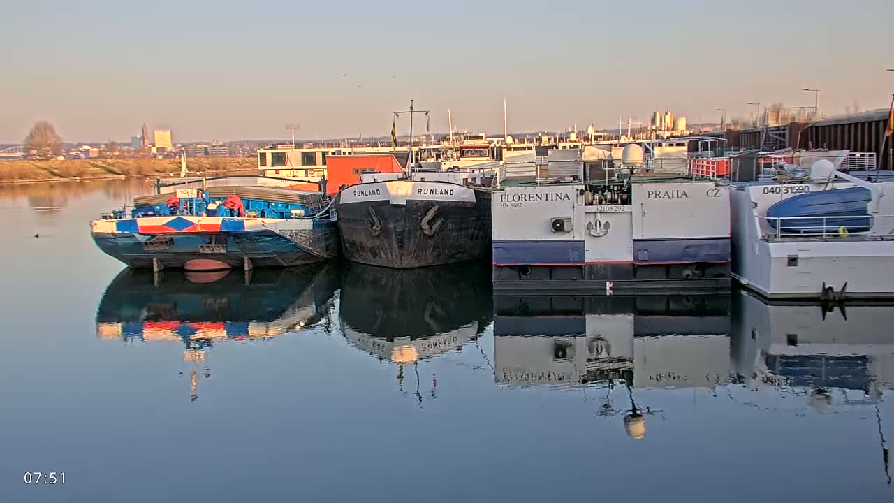 Several barges are moored along a calm river under a clear, pale sky.