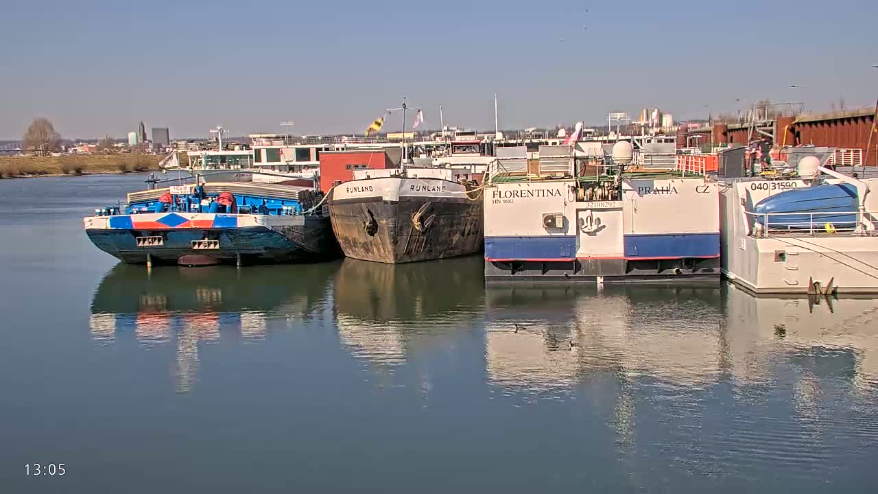 Several barges are moored along a calm river under a clear blue sky.