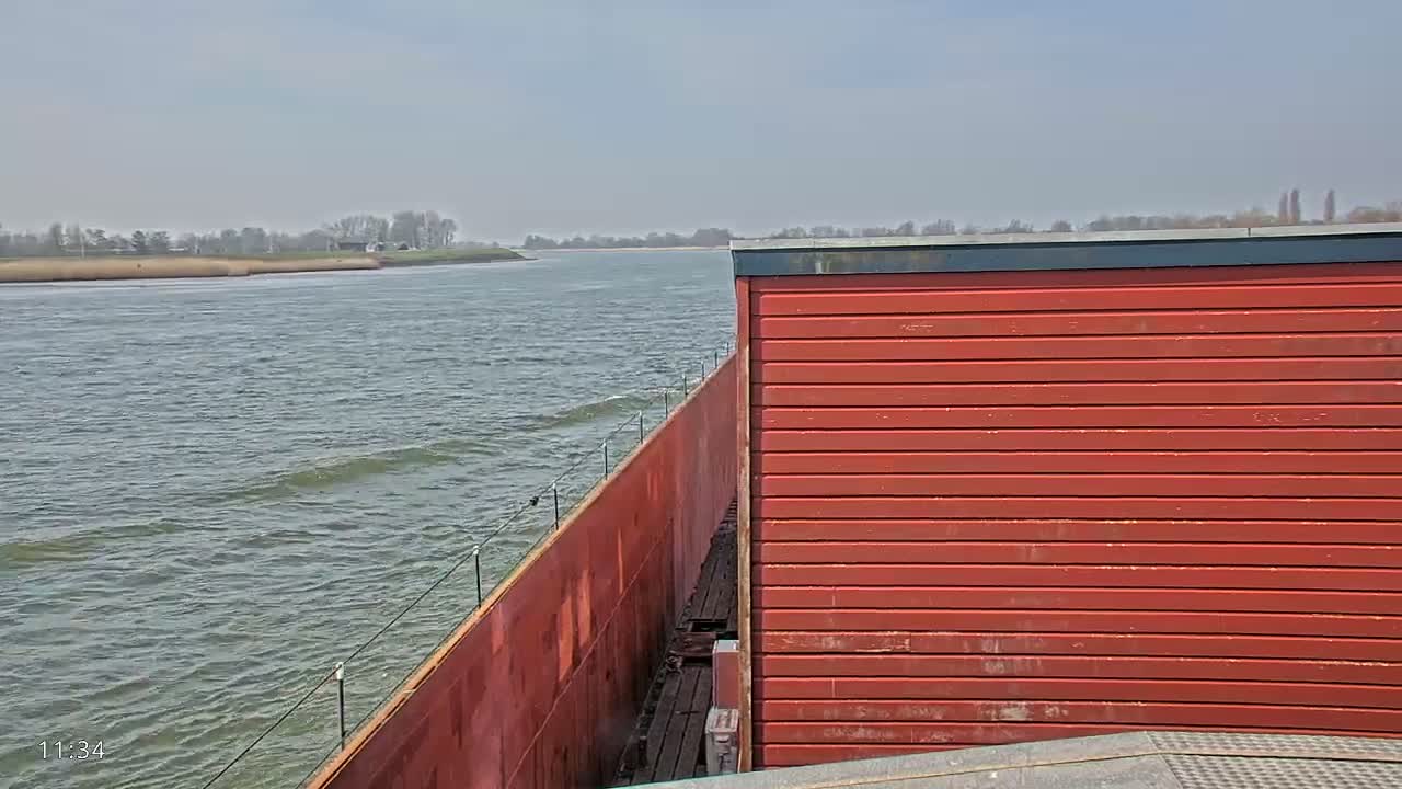 A red structure on a barge moves across a body of water under a partly cloudy sky.