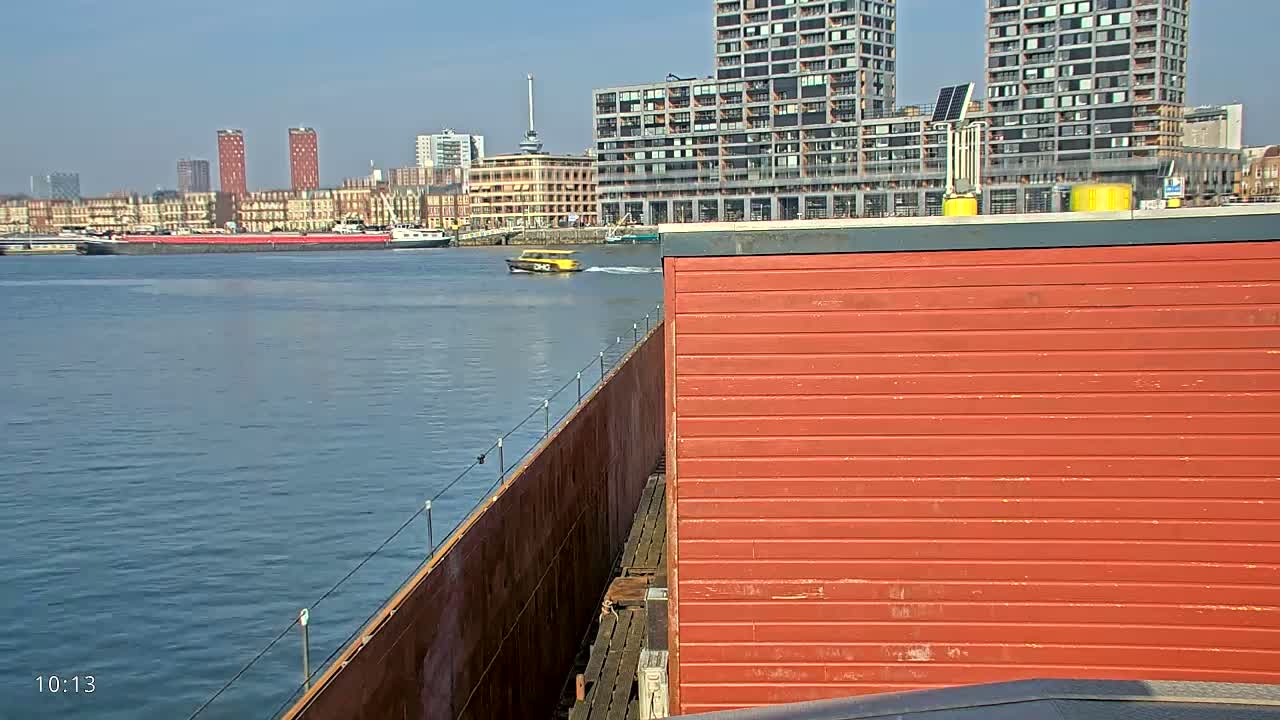 A waterway with a barge and a small yellow boat visible, under a clear sunny sky, with modern buildings in the background.