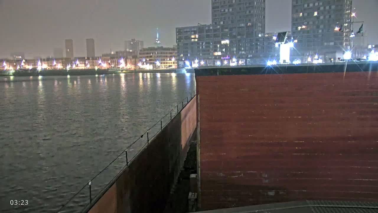 A nighttime view of a dark body of water reflecting lights from a city skyline under an overcast sky.