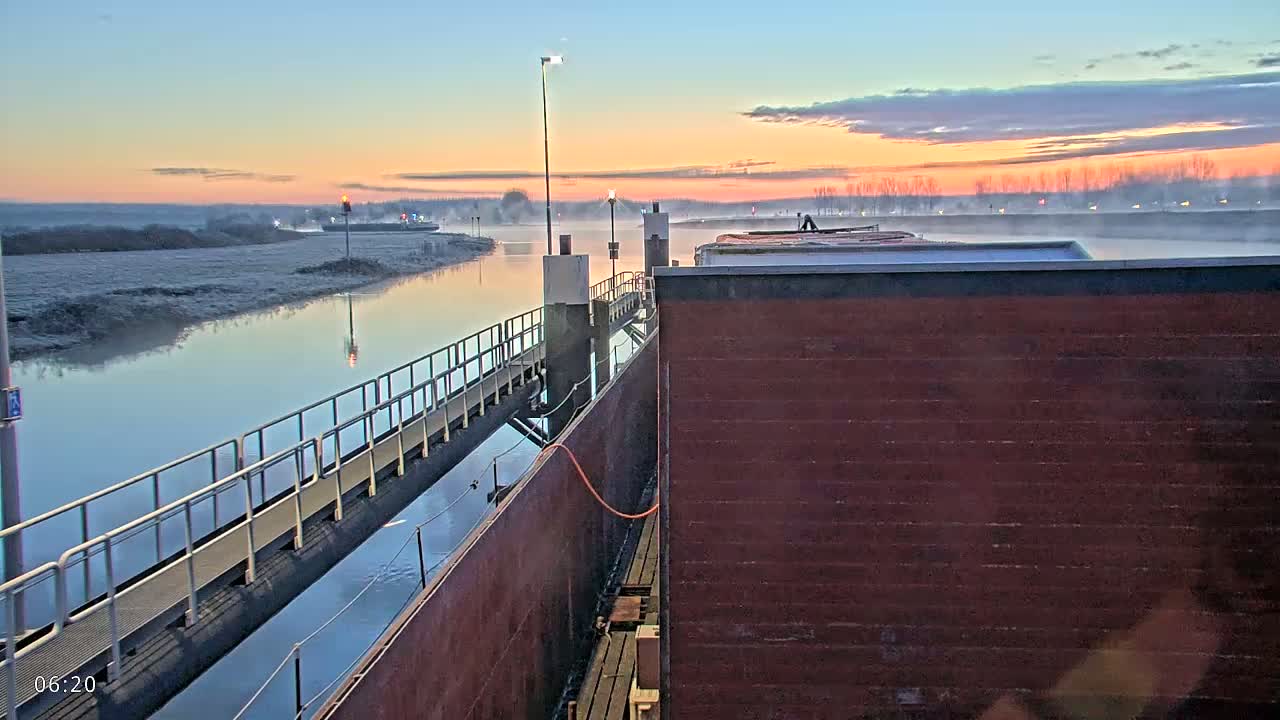 A barge is docked at a lock on a calm river at sunrise, with frost visible on the riverbank.