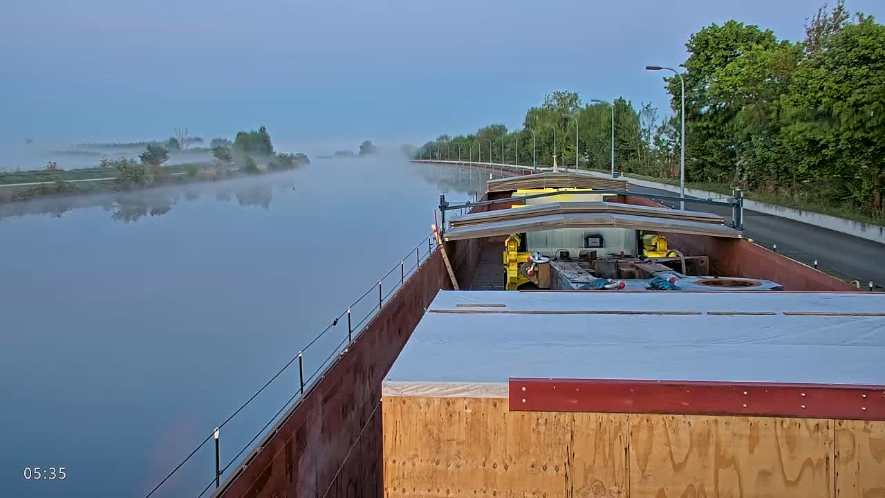 A barge carrying cargo is moored on a foggy canal at dawn.