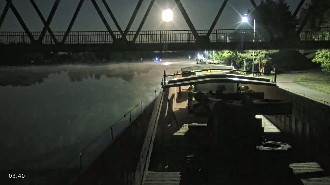 A barge travels under a bridge at night on a foggy waterway illuminated by a bright moon.