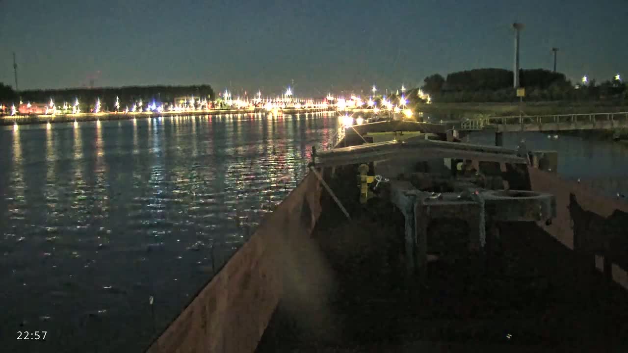 A barge travels at night on a waterway past a shoreline illuminated with lights.