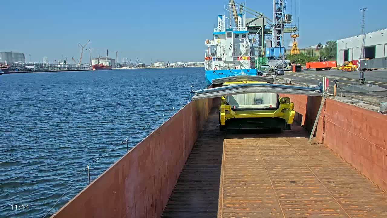 A yellow piece of heavy machinery sits on a barge in a harbor on a sunny day.