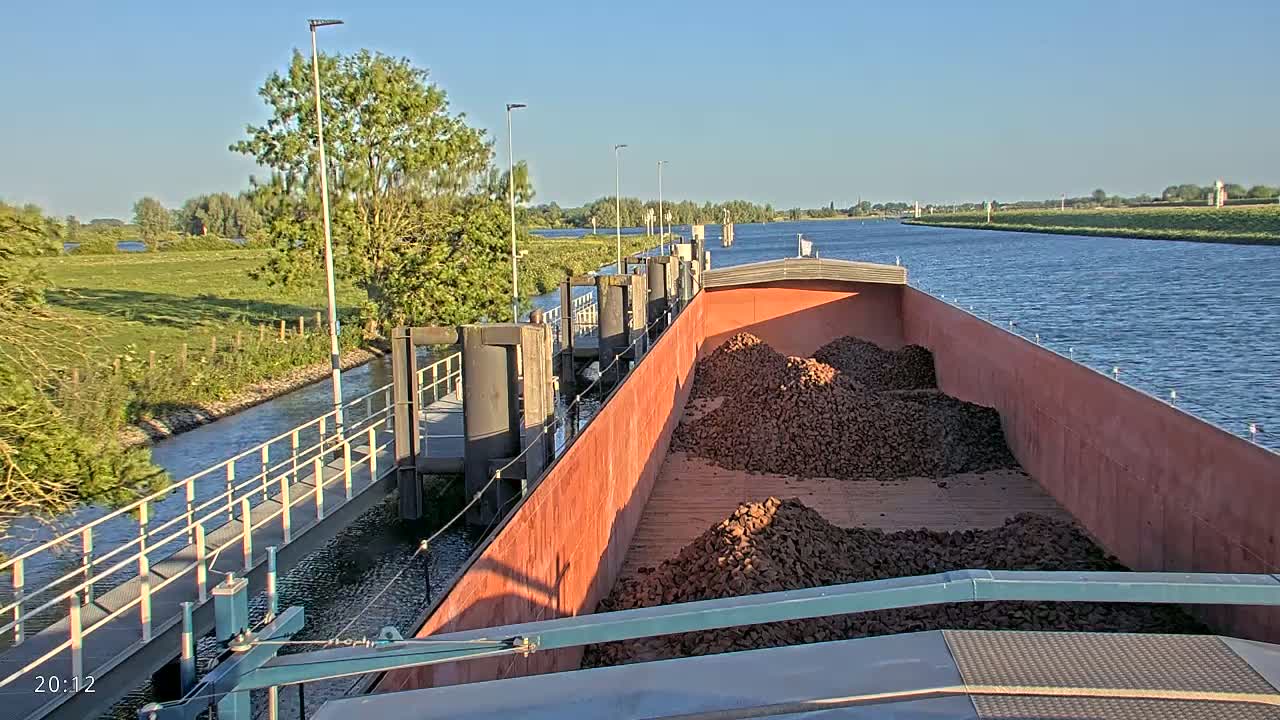 A barge loaded with a large quantity of dark-colored rocks is traveling down a canal on a sunny day.