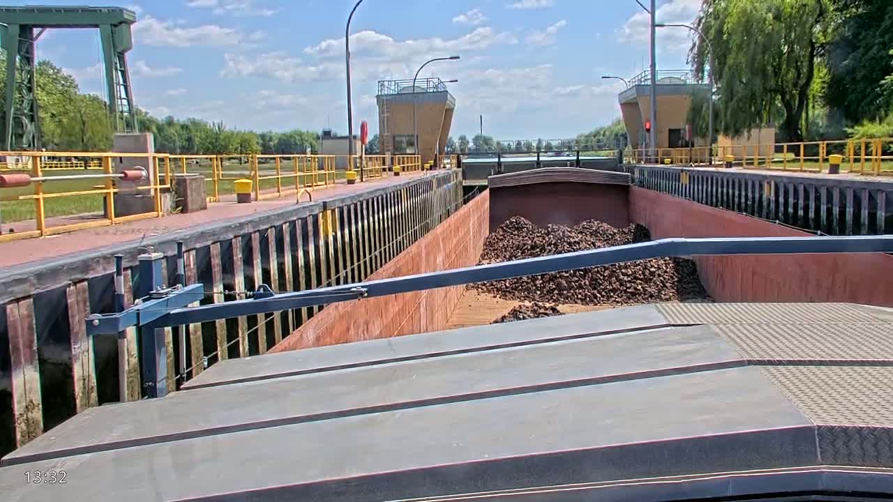 A barge filled with dark, granular material is positioned inside a canal lock under a partly cloudy sky.