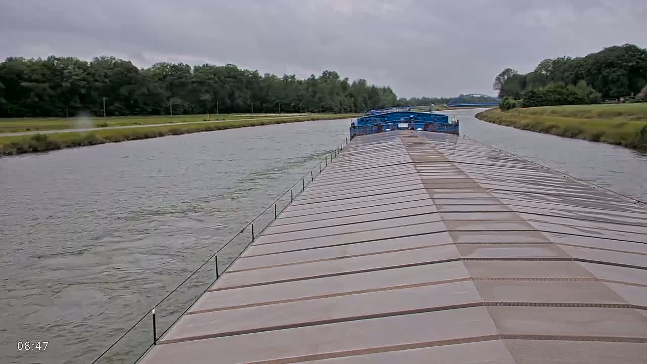 A barge travels down a canal under an overcast sky, another barge visible ahead.