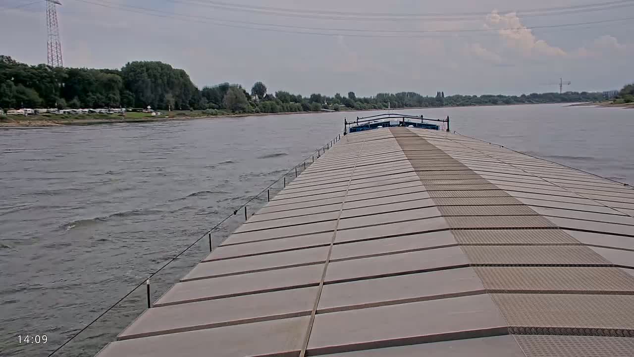 A barge travels down a river on a partly cloudy day, with a slight chop on the water's surface.