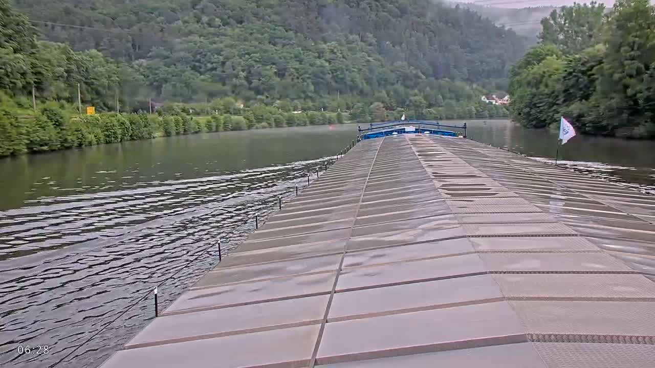 A barge travels down a river surrounded by lush green hills under a calm sky.
