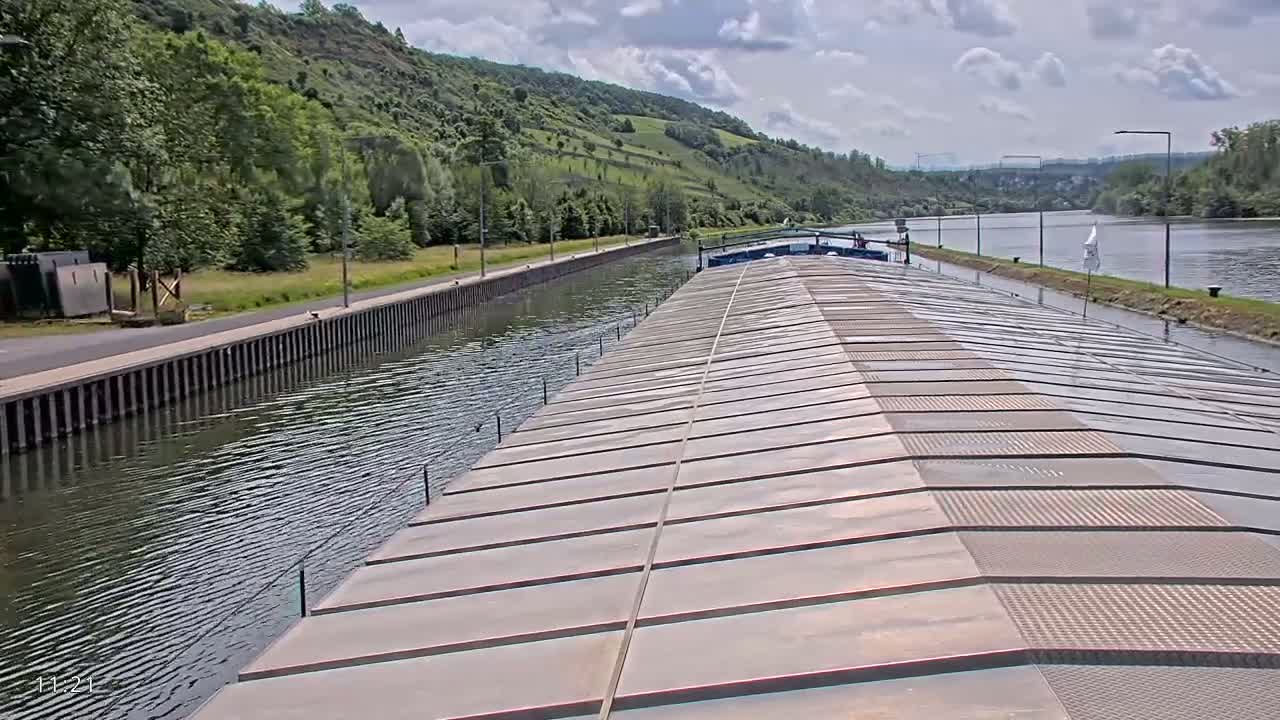 A barge travels down a canal on a partly cloudy day, with green hills visible in the background.